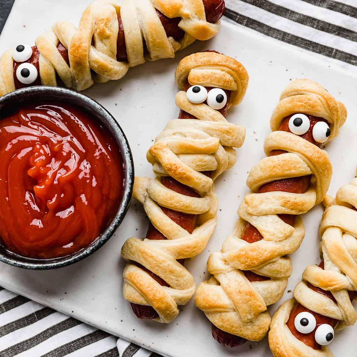 Mummy hot dogs wrapped in golden crescent dough with candy eyes, easy Halloween party snacks kids can help make