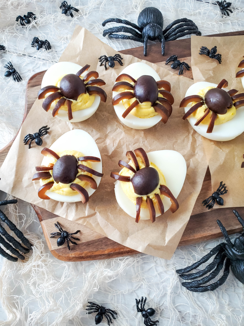 Deviled eggs topped with black olive spiders on a serving plate
