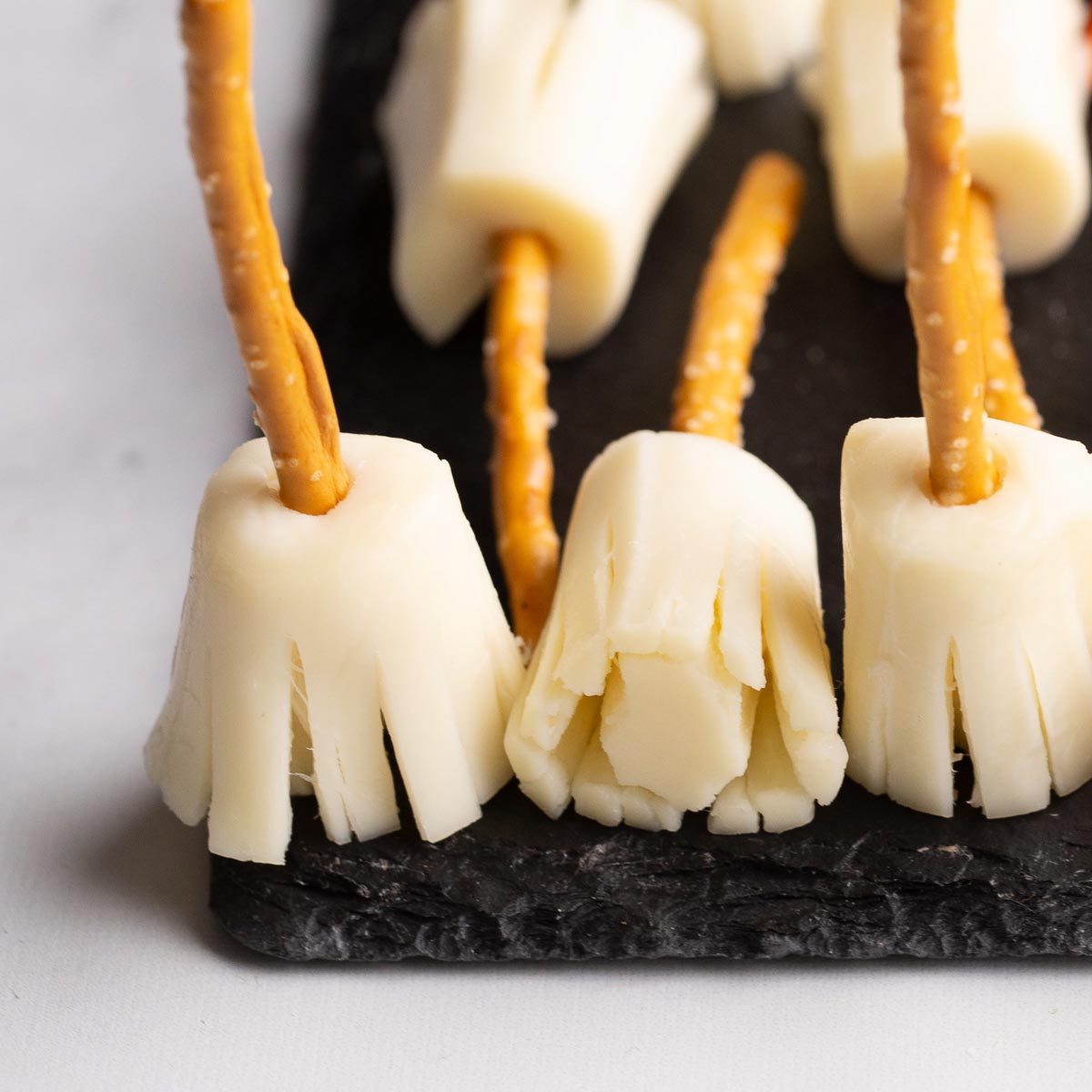 String cheese broomsticks with pretzel handles fanned out on a plate