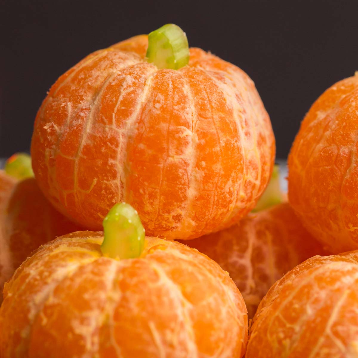 Peeled clementines with small green stems arranged as tiny pumpkins