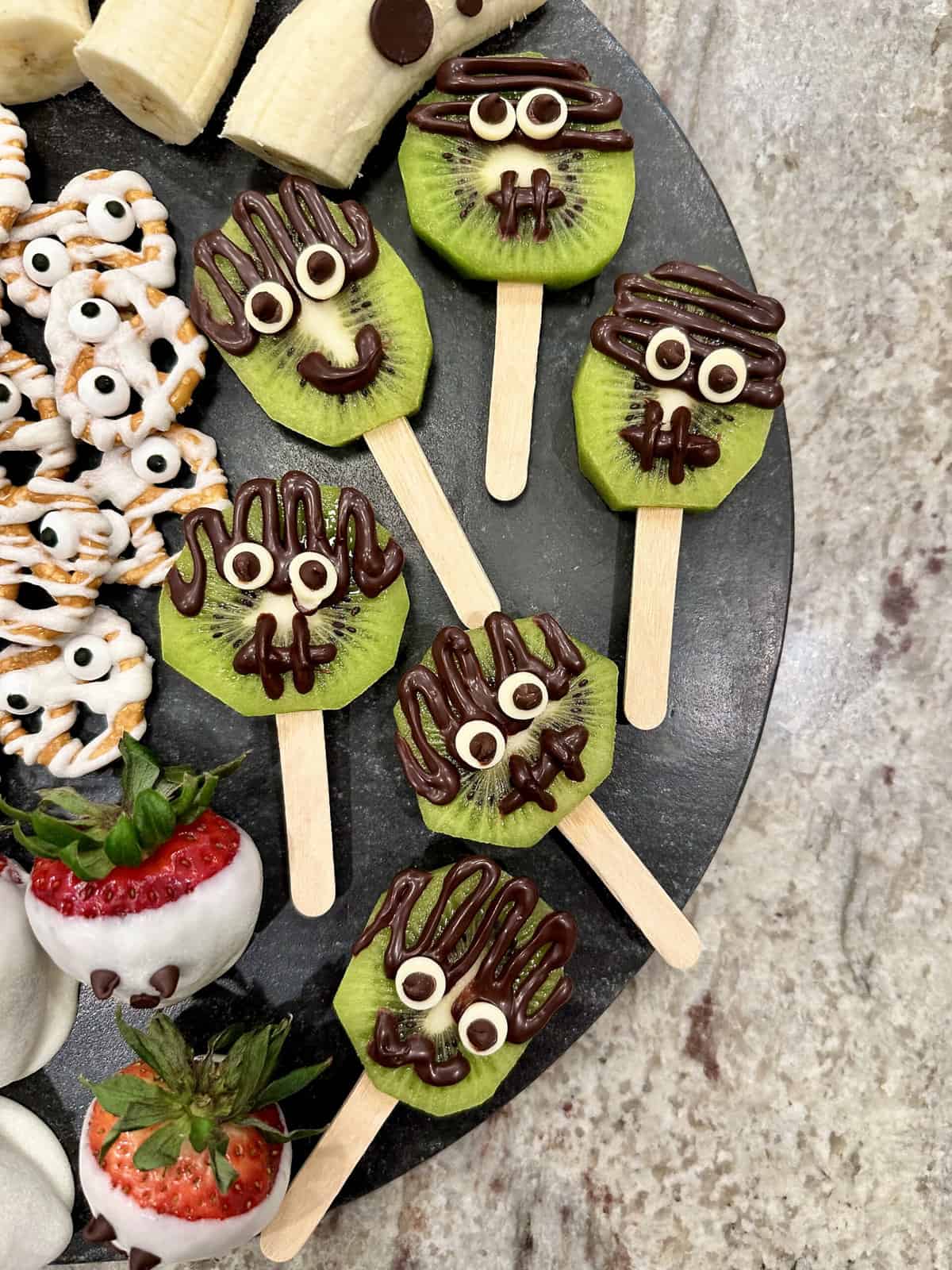 Kiwi slices on sticks decorated as Frankenstein faces with chocolate hair and candy eyes