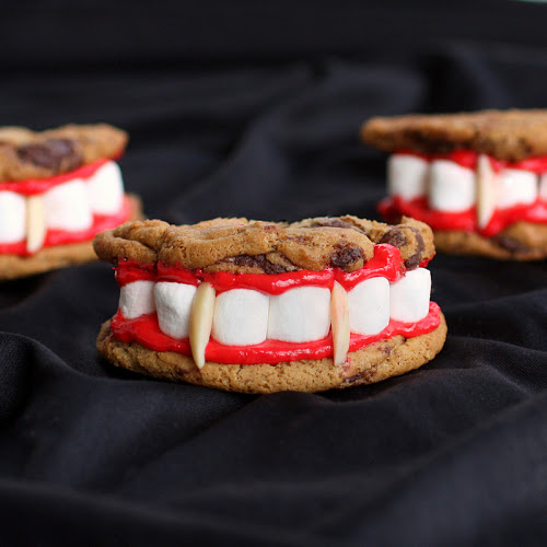 Cookie sandwiches with red frosting, mini-marshmallow teeth and almond fangs arranged as vampire mouths on dark cloth