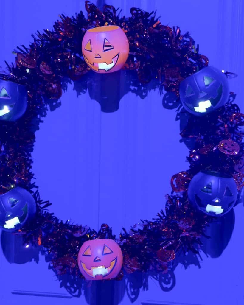 Glowing pumpkin bucket wreath with orange and dark pumpkin pails hanging on a door