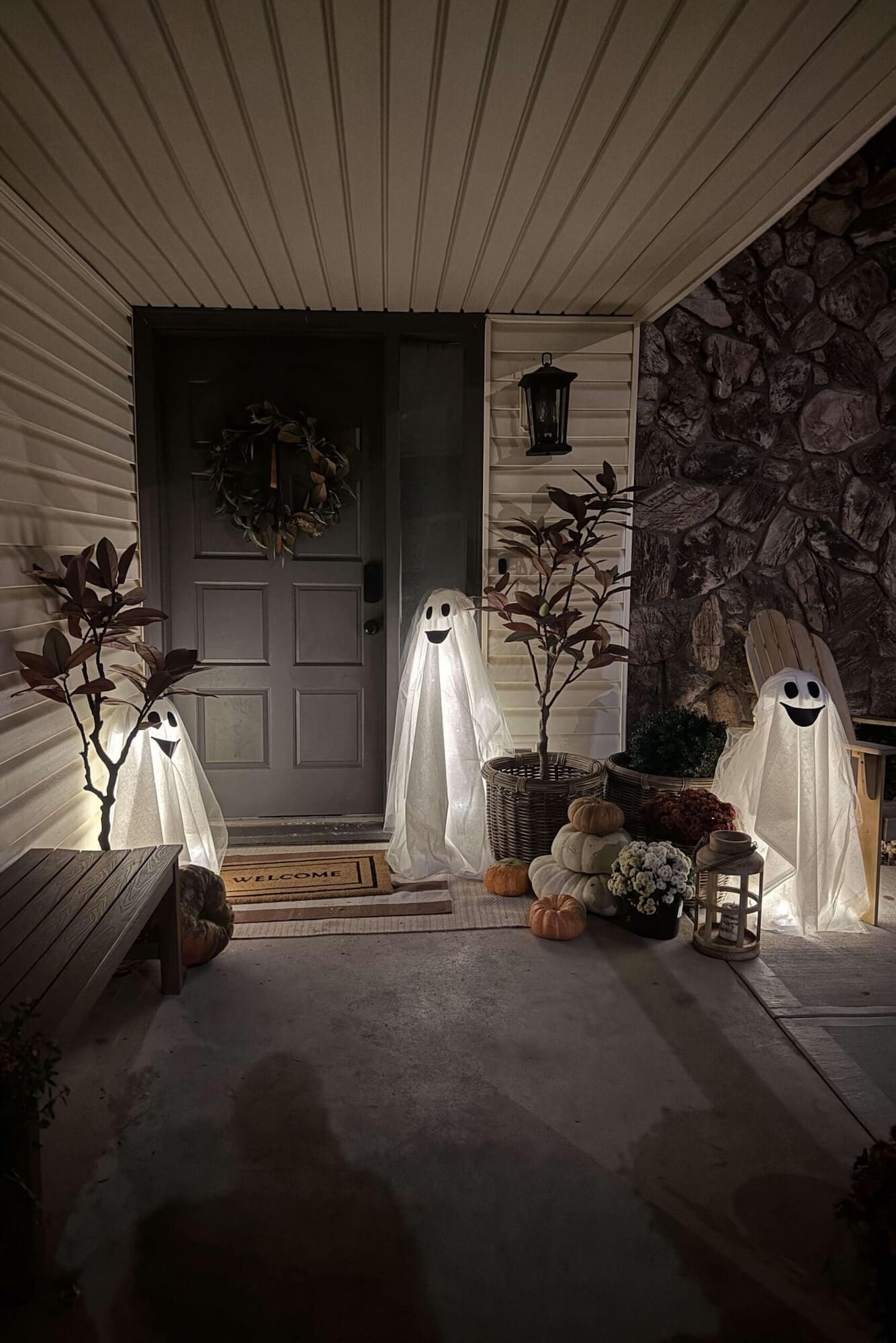Three light up tomato cage ghosts with smiling faces on a front porch at night