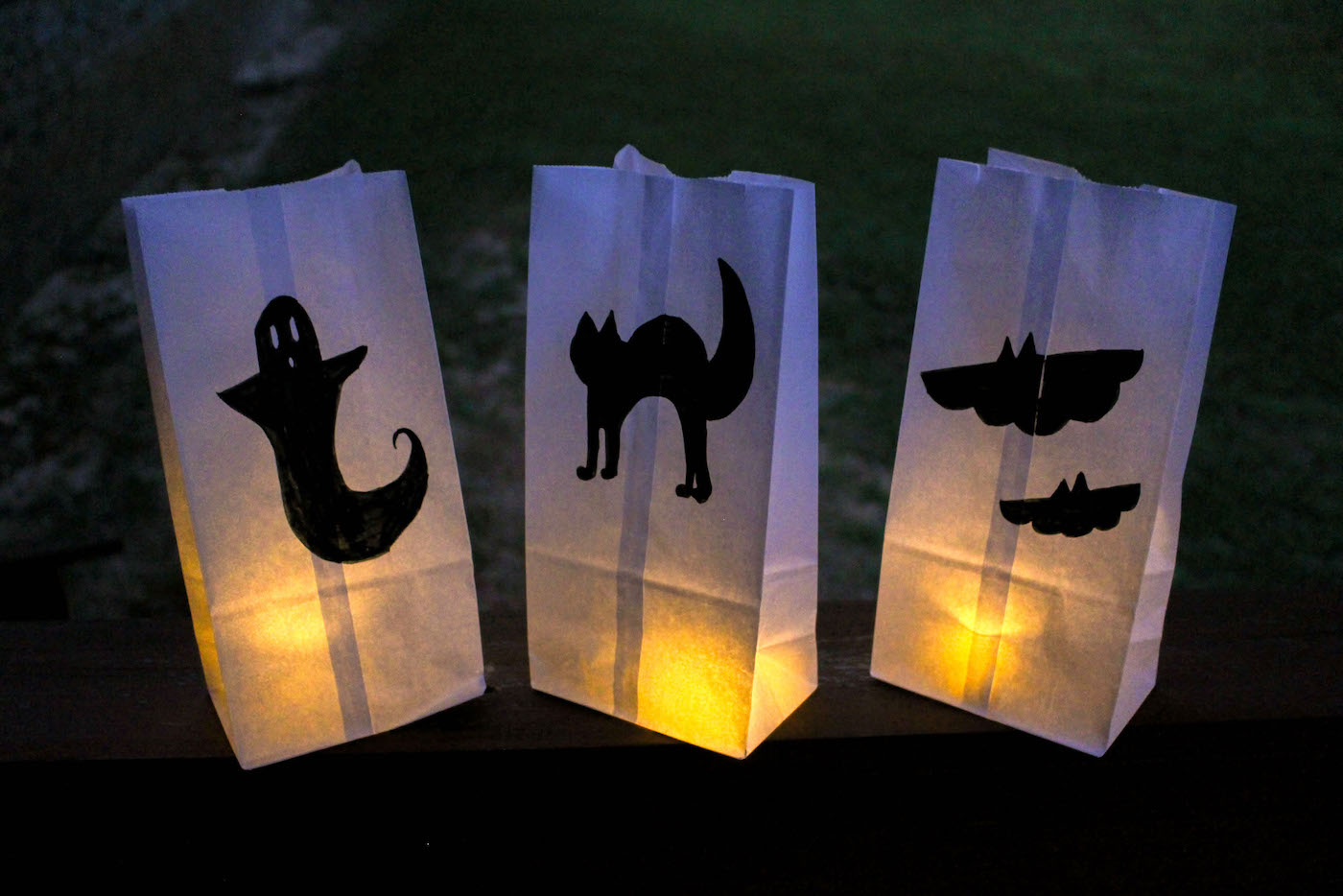 Three paper-bag lanterns glowing on an outdoor ledge