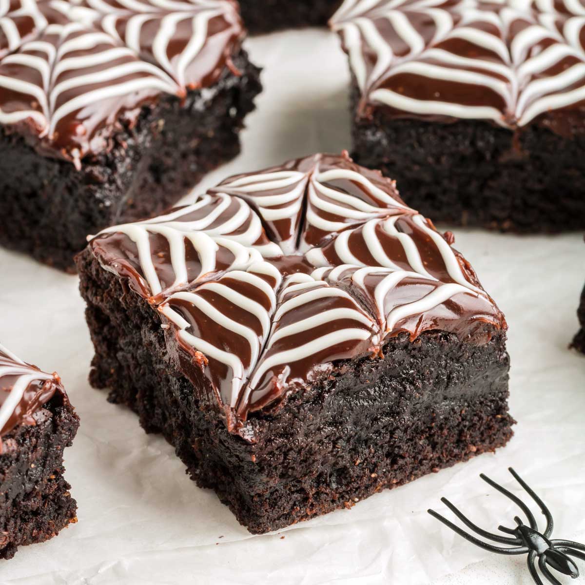 Spiderweb brownies with a piped white web over dark frosting
