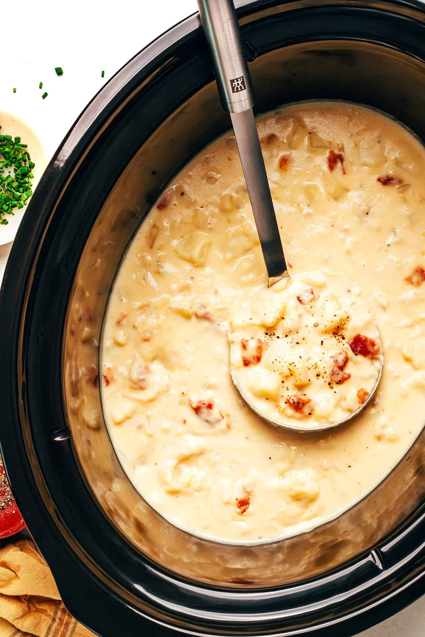 Potato soup cooking in a slow cooker with a ladle