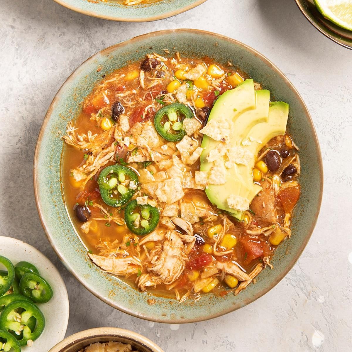 Chicken tortilla soup with avocado slices, corn and jalapeno