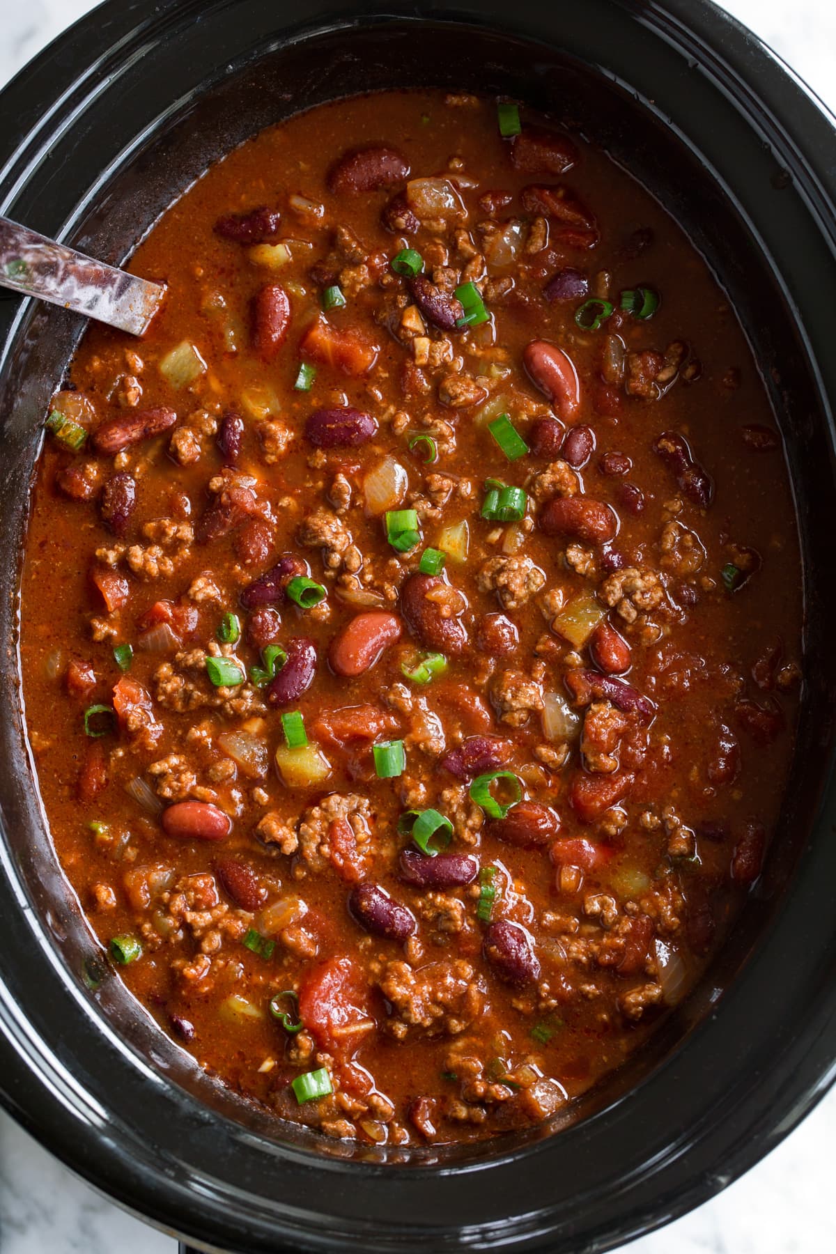 Beef and bean chili in a slow cooker topped with green onions